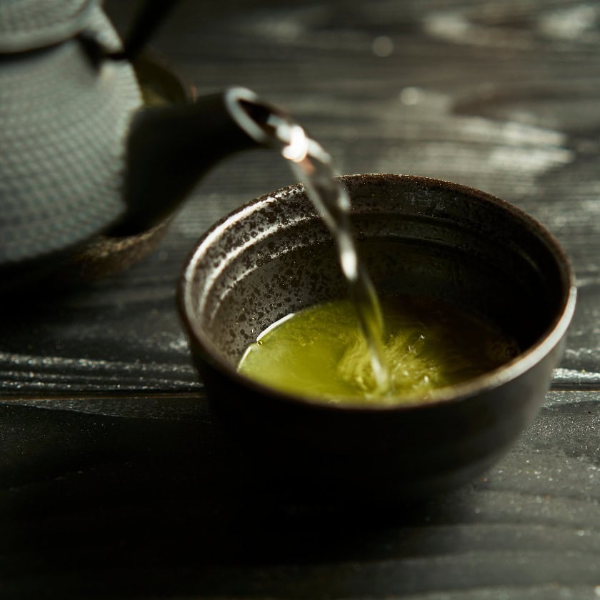 Japanischer Bio-Matcha-Grüntee in Tasse auf schwarzem Holzhintergrund. Gesundes Produkt aus der Natur, typisch für die orientalische Tradition. Japanische Teezeremonie.